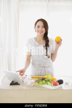 Jeune femme japonaise attrayant cooking at home with tablet Banque D'Images