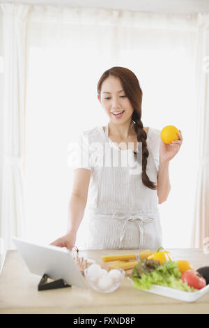 Jeune femme japonaise attrayant cooking at home with tablet Banque D'Images