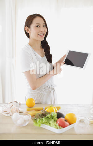 Jeune femme japonaise attrayant cooking at home with tablet Banque D'Images
