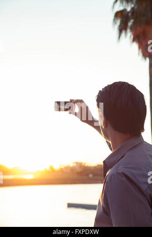 Man photographing sunset with smartphone Banque D'Images