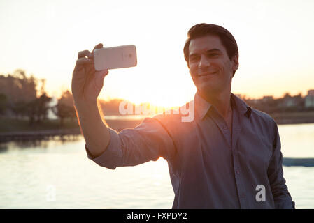 Man using smartphone pour photographier lui-même devant le coucher du soleil Banque D'Images