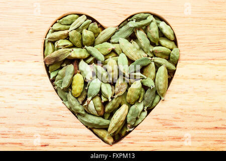 Cardamome verte en forme de coeur en bois tas sur fond de table rustique Banque D'Images