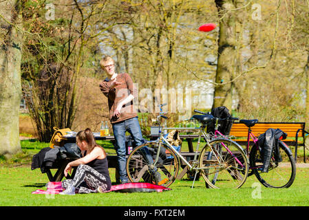 Lund, Suède - 11 Avril 2016 : tous les jours la vie en ville. Young adult man dans un parc est de lancer un disque volant tandis qu'une femme siège à fro Banque D'Images