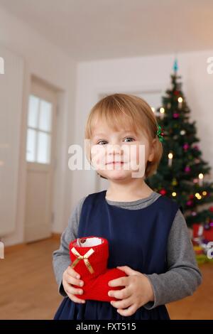 Girl in front of Christmas Tree holding red boot looking at camera smiling Banque D'Images