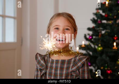 Girl in front of Christmas Tree holding sparkler smiling at camera Banque D'Images