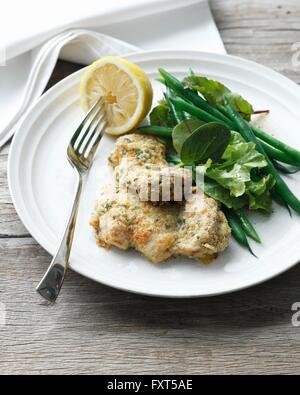 Assiette de farine de poulet avec les morceaux de poulet en croûte, haricots verts, salade mesclun et citron Banque D'Images