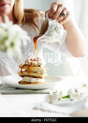 Woman pouring sauce caramel orné de pot sur pile de pikelets Banque D'Images