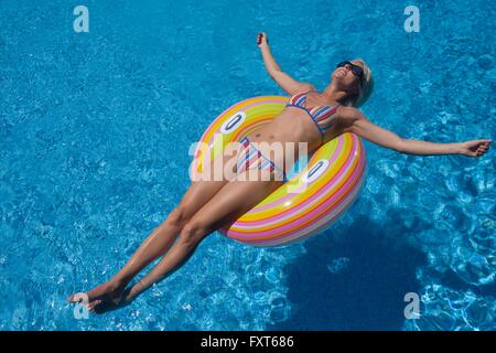 Young woman wearing bikini sunbathing on inflatable ring in swimming pool Banque D'Images