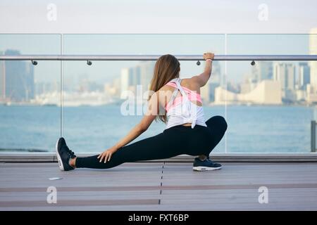 Vue arrière du jeune femme exerçant et en étirant les jambes sur le bord de mer, Hong Kong Banque D'Images