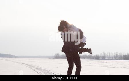 Young man carrying woman sur le terrain couvert de neige Banque D'Images