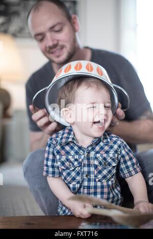 Père de placer dans une passoire sur la tête des garçons smiling baby Banque D'Images