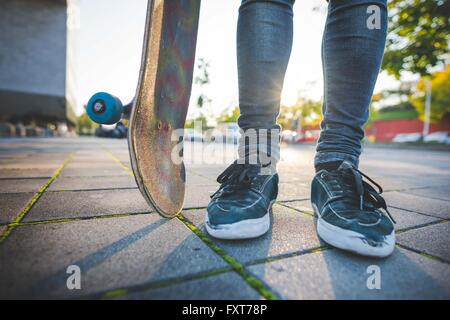 Les jambes et les pieds des hommes jeunes skateboarder urbain debout sur un trottoir Banque D'Images