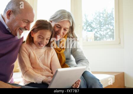 Les grands-parents sur la fenêtre à l'aide de tablette numérique avec sa petite-fille à bas smiling Banque D'Images