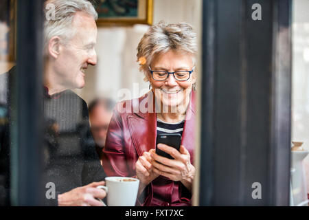 Senior couple sitting at cafe siège de fenêtre de boire du café et texting on smartphone Banque D'Images