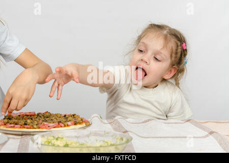 Petite fille avec la langue qui sort d'une main pour tirer la pizza, qui prépare sa grande soeur Banque D'Images