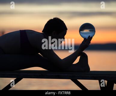 Woman practicing yoga par lac au coucher du soleil Banque D'Images