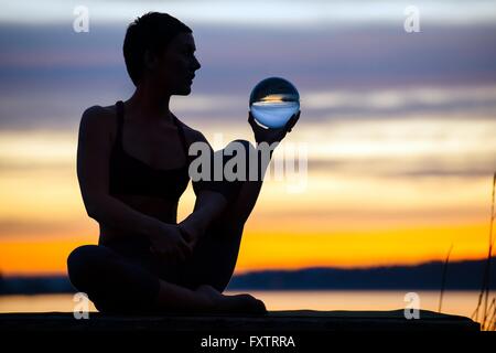 Woman practicing yoga par lac au coucher du soleil Banque D'Images