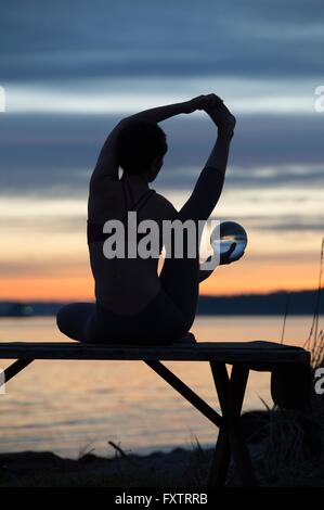 Woman practicing yoga par lac au coucher du soleil Banque D'Images