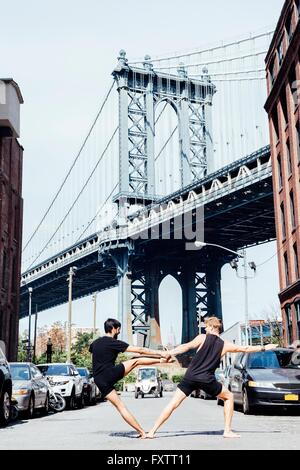 Deux hommes de vous pencher sur le côté en position de yoga en face du pont de Manhattan, New York, USA Banque D'Images