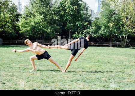 Deux hommes de vous pencher sur le côté en position de maintien de pied de yoga in park Banque D'Images