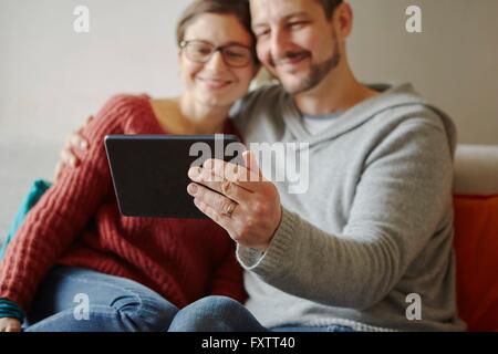 Young couple sitting on sofa with digital tablet selfies en tenant Banque D'Images