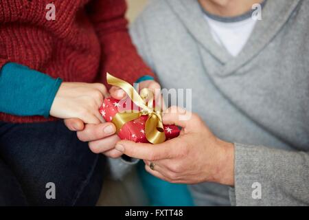 Close up of couple holding hands and xmas gift on sofa Banque D'Images