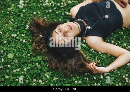 Portrait de femme avec anneau dans le nez allongé sur clover couverts d'herbe, les yeux fermés Banque D'Images