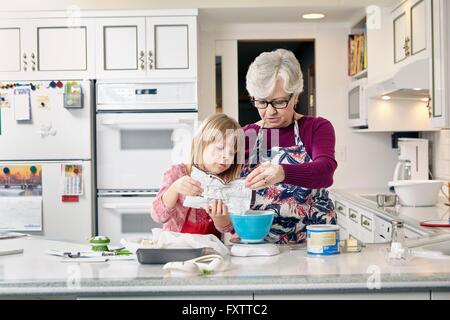 Fille et grand-mère de verser le mélange à gâteau au comptoir de la cuisine Banque D'Images