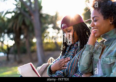 Female friends relaxing in park, le partage d'écouteurs Banque D'Images