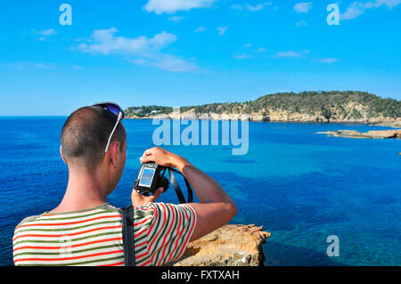 Libre d'un jeune homme de race blanche vue de derrière en prenant une photo de la mer Méditerranée et la côte de l'île d'Ibiza, Espagne Banque D'Images