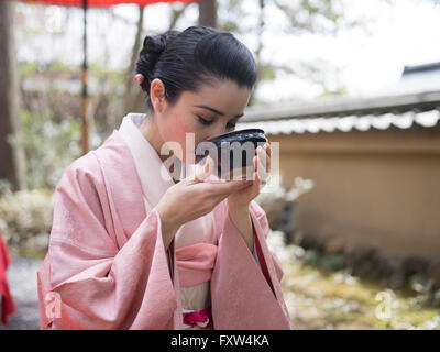 Femme japonaise en kimono de boire un bol de thé vert dans les jardins du Temple Kinkaku-ji, un temple bouddhiste Zen à Kyoto, au Japon. Banque D'Images