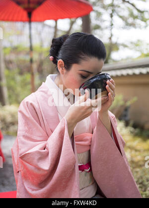 Femme japonaise en kimono de boire un bol de thé vert dans les jardins du Temple Kinkaku-ji, un temple bouddhiste Zen à Kyoto, au Japon. Banque D'Images