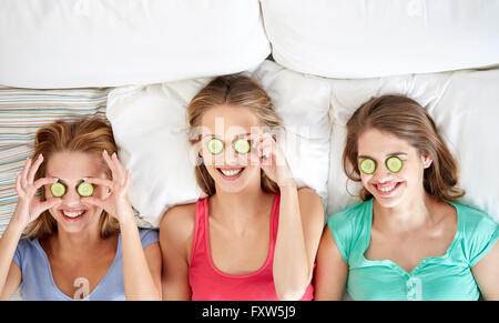 Heureux les jeunes femmes avec masque de concombre au lit Banque D'Images