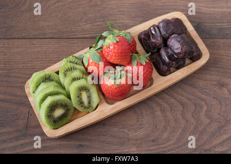 Fraises, kiwis et les dates dans un plateau en bambou. Fruits frais et fruits secs plateau. Salade de fruits. Banque D'Images