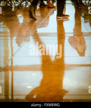 Réflexions de silhouettes de jambes, pieds et les parties du corps des voyageurs dans un aéroport /hall de gare. Des couleurs chaudes. Banque D'Images