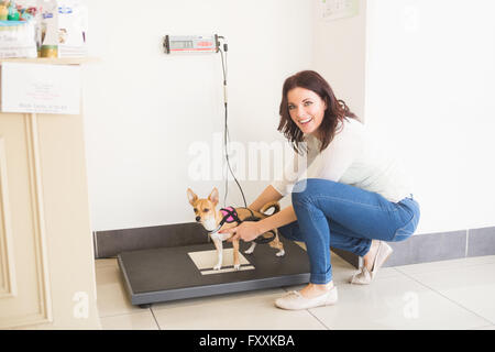 Heureux femme pesant son chien sur une balance vétérinaire Banque D'Images