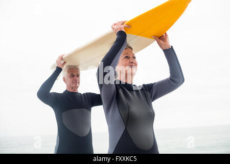 Senior couple in wetsuit surf transport over head Banque D'Images