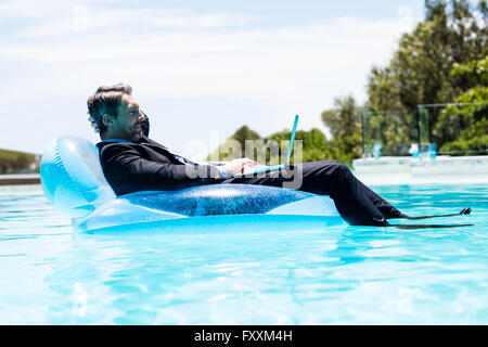 Businessman using laptop on inflatable Banque D'Images