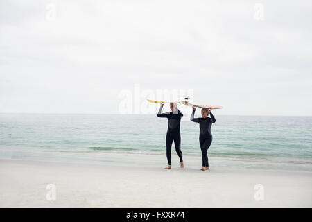 Senior couple in wetsuit surf transport over head Banque D'Images