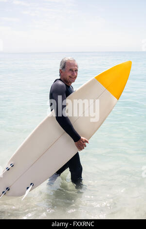 Happy senior man in wetsuit holding a surfboard Banque D'Images