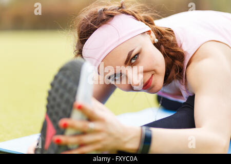 Jeune fille sportive doing stretching sur Tapis de fitness. La sportive attrayante à la caméra et s'étend à l'extérieur Banque D'Images