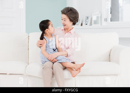Grand-mère tenant sa petite-fille assis sur un canapé et se regardant avec un sourire Banque D'Images