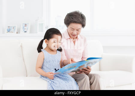 Grand-mère de lire un livre à sa petite-fille à la fois assis sur un canapé Banque D'Images