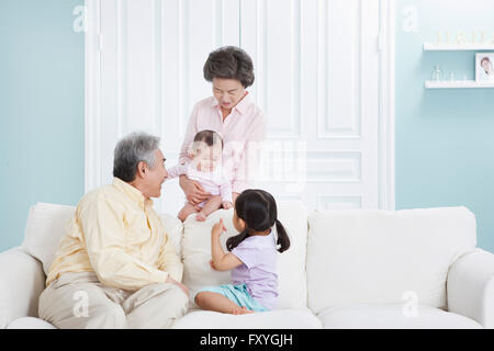 Grand-mère tenant un bébé derrière un canapé et un grand-père avec sa petite-fille assis sur un canapé et regardant le bébé avec un sourire Banque D'Images