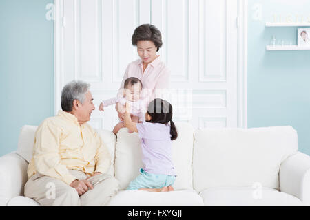 Grand-mère tenant un bébé derrière un canapé et un grand-père avec sa petite-fille assis sur un canapé et regardant le bébé avec un sourire Banque D'Images