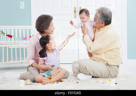 Grand-père tenant un bébé et grand-mère et sa petite-fille à la recherche à l'ensemble de bébé assis sur le plancher Banque D'Images