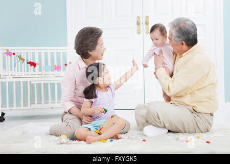 Grand-père tenant un bébé et grand-mère et sa petite-fille à la recherche à l'ensemble de bébé assis sur le plancher Banque D'Images