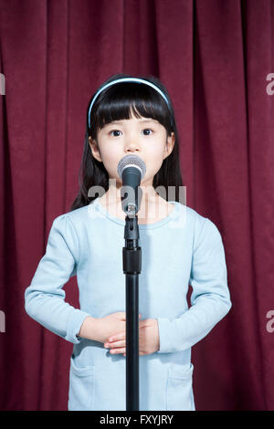 Girl singing derrière un microphone permanent sur la scène Banque D'Images