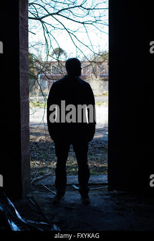 Silhouette d'un homme aux portes d'un bâtiment abandonné Banque D'Images