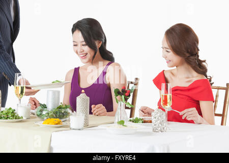 Jeune homme donnant un plat pour les jeunes femmes sitting at table Banque D'Images